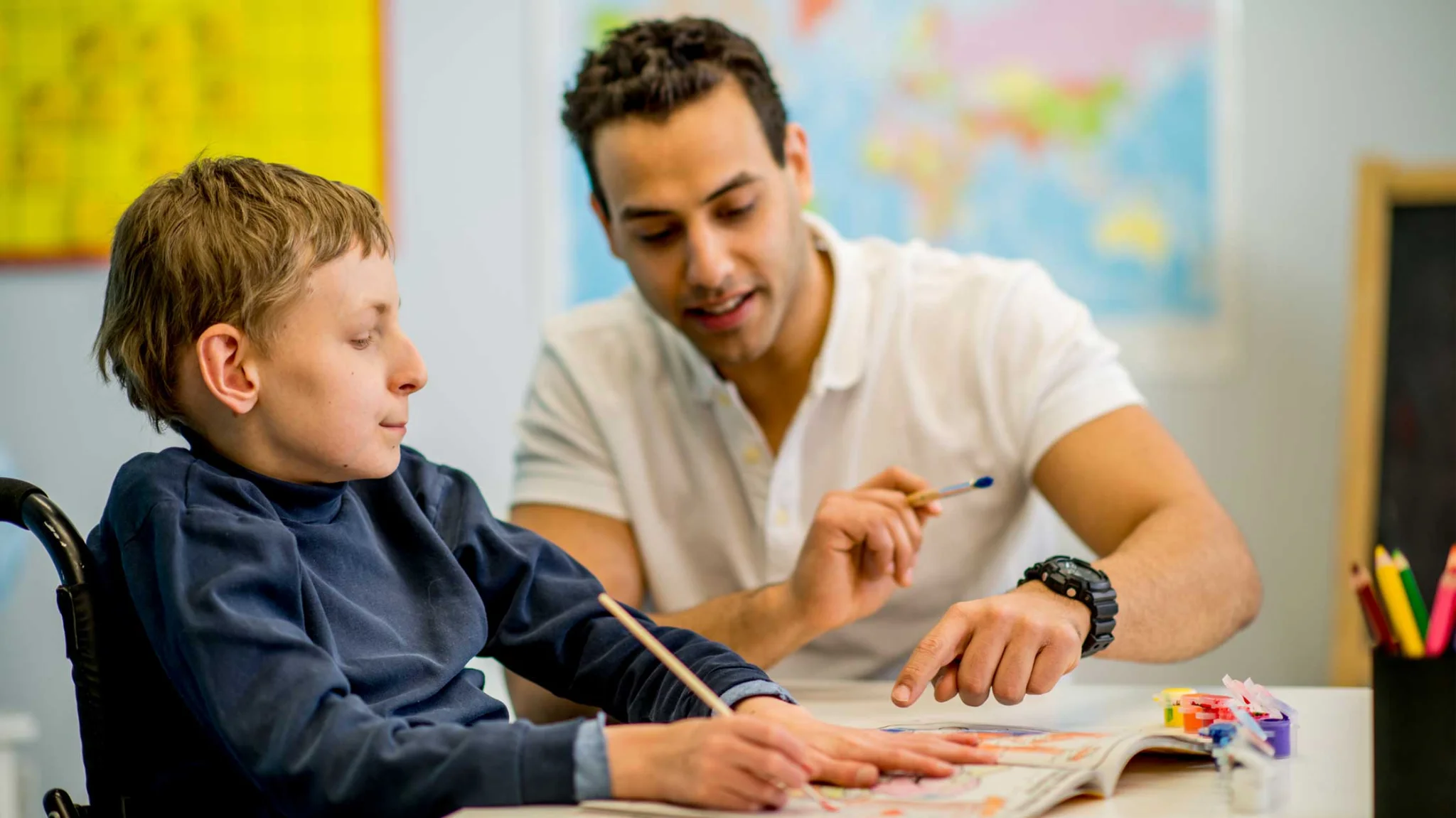 A teacher helping a boy color in a coloring book