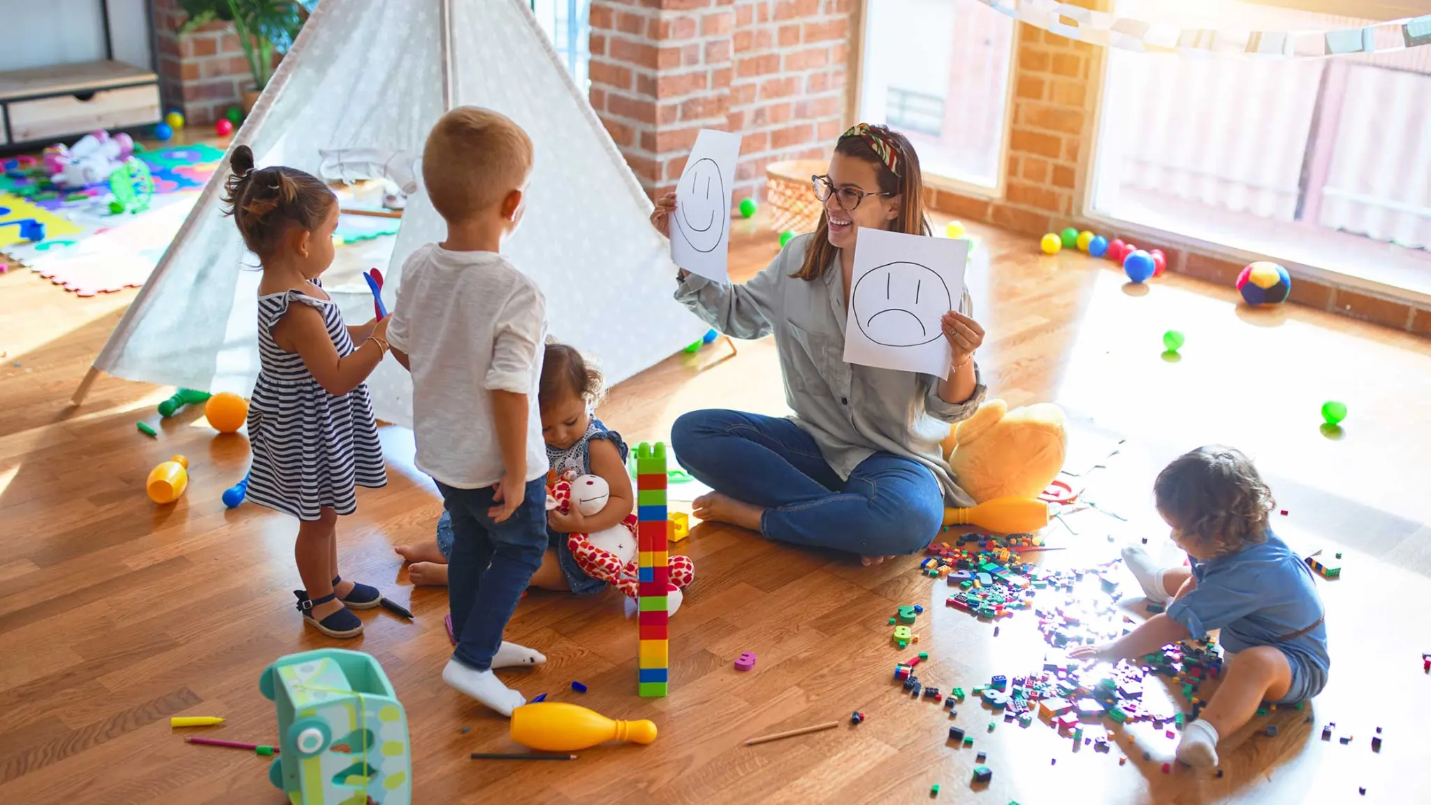 A woman holding up a smiling face and a frowning face for the children to learn emotions