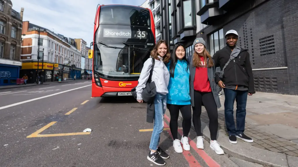 Four students wait in front of a bus in London