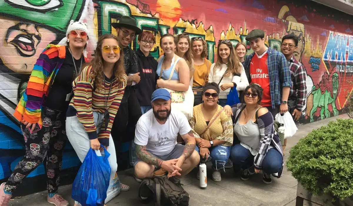 Fourteen First-Year Study Abroad students standing in front of a mural outside and smiling at the camera