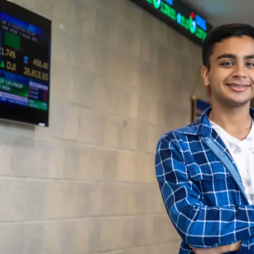 A business student stands in front of a stock ticker.