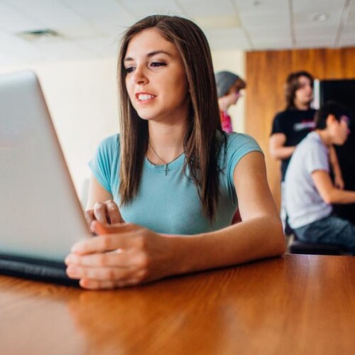 Person at table with laptop, others behind her around a piano