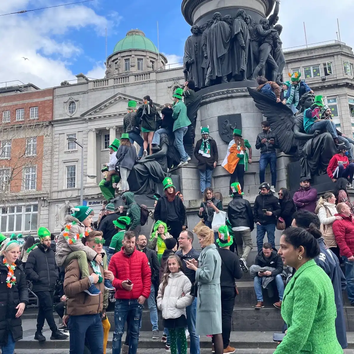 People stand on the steps of a monument dressed in green and wearing leprechaun hats