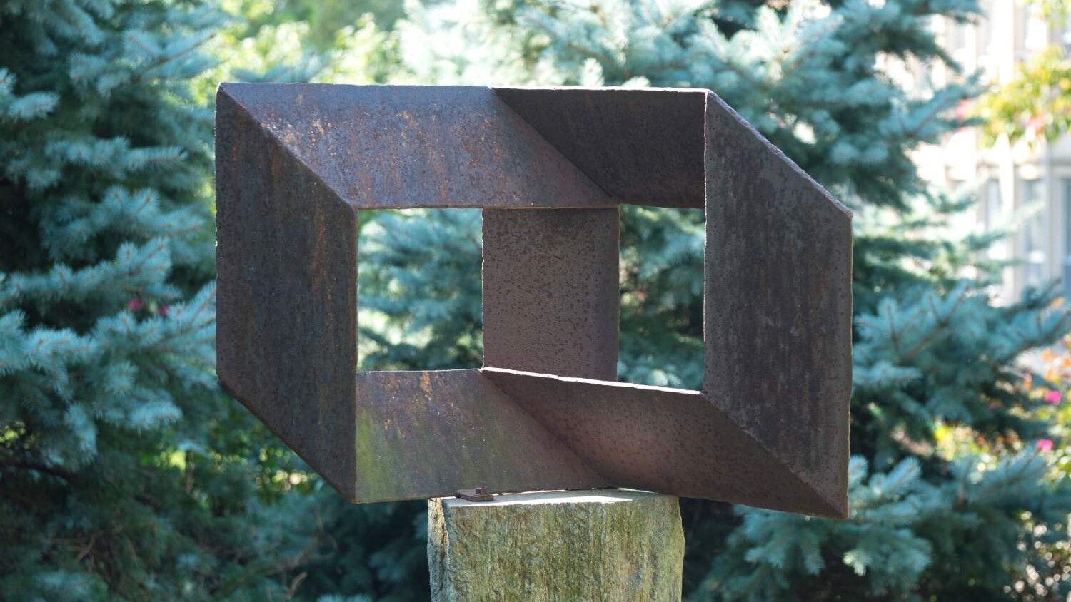 a rectangular metal sculpture with a pine tree in the background