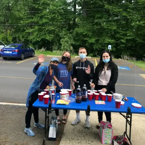 A group of students wearing masks stands in front of a table with red cups and bottles of soda