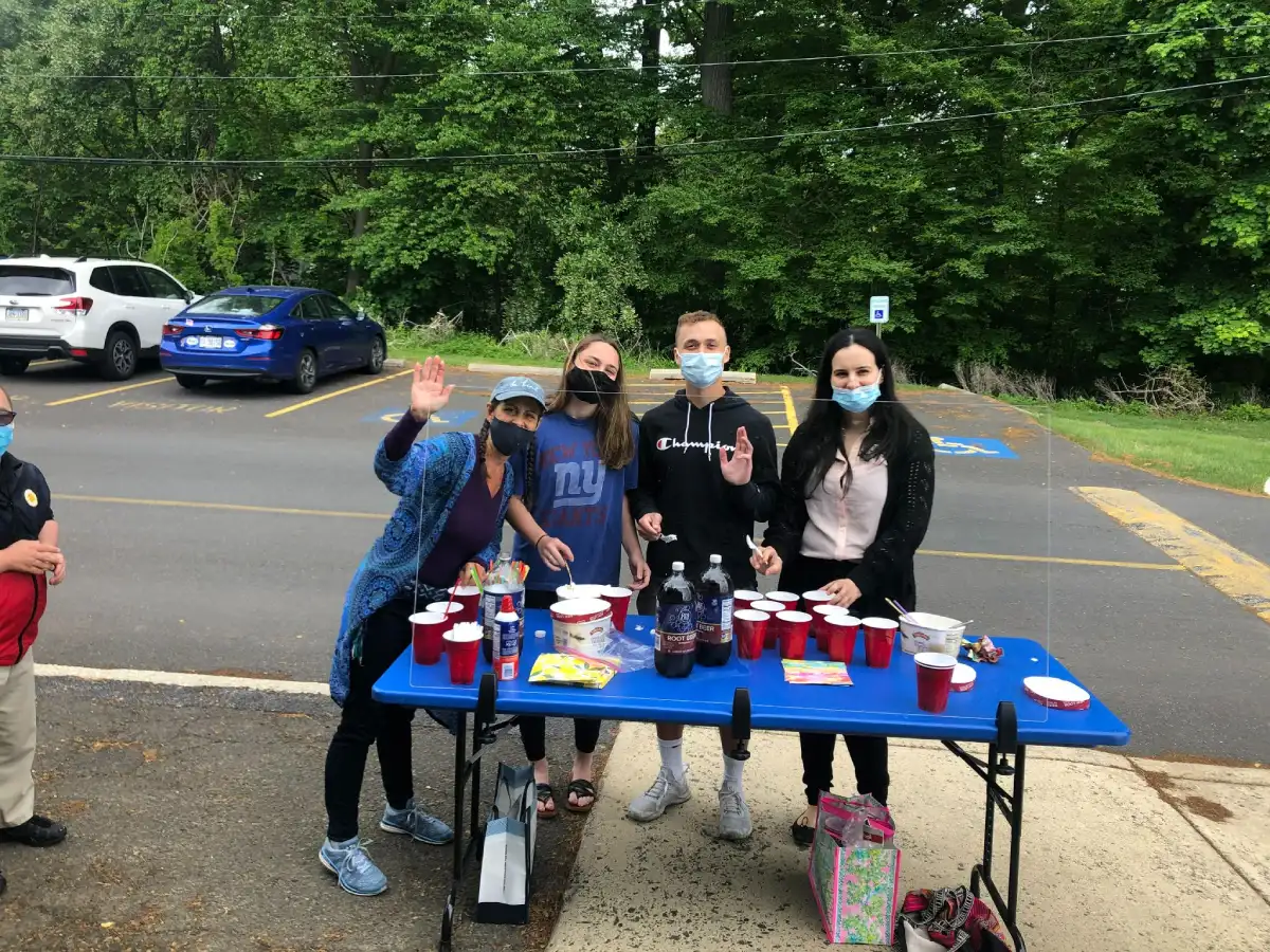 A group of students wearing masks stands in front of a table with red cups and bottles of soda