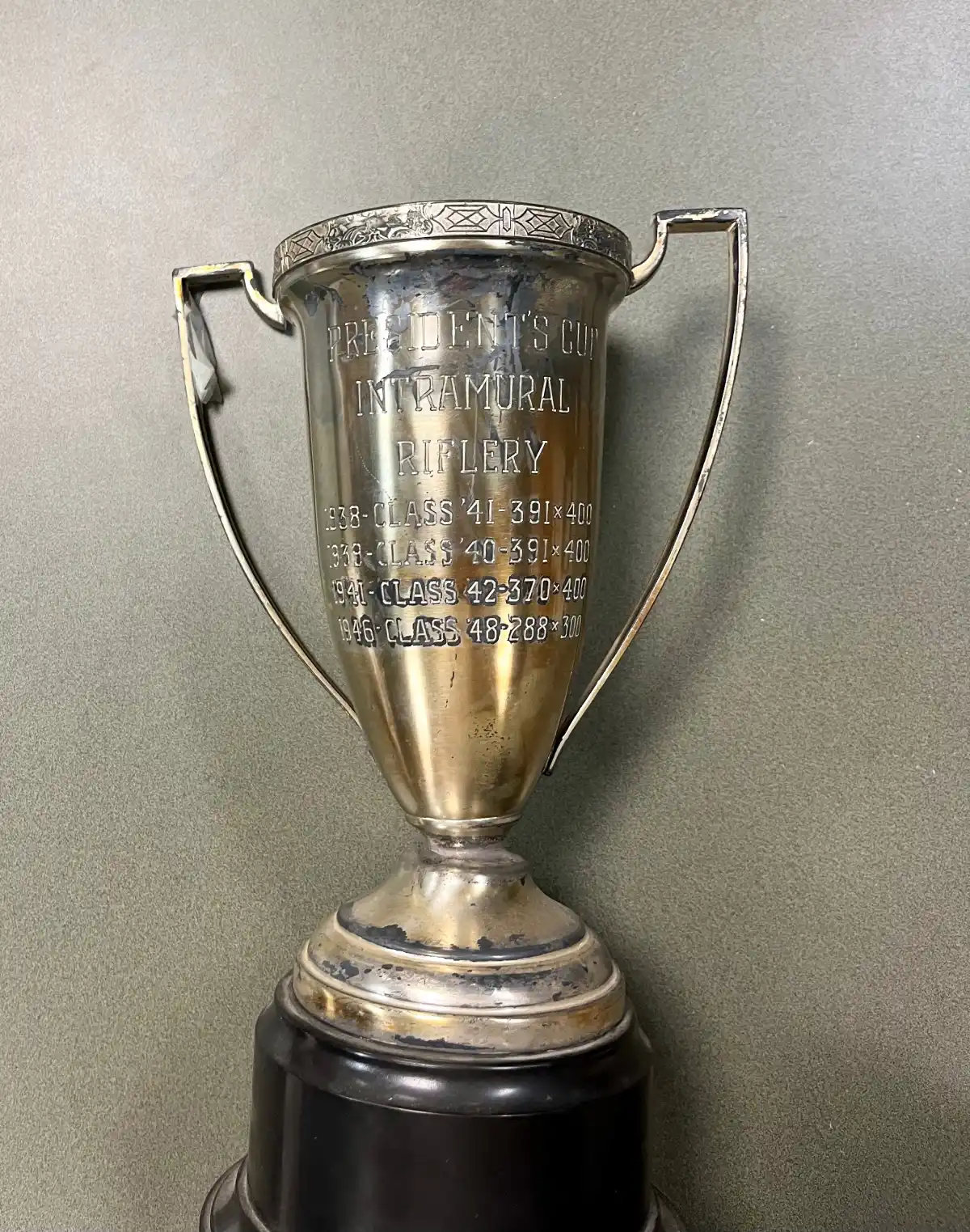 An aged silver trophy is engraved with "President’s Cup Intramural Riflery Trophy dating from 1938-1948."