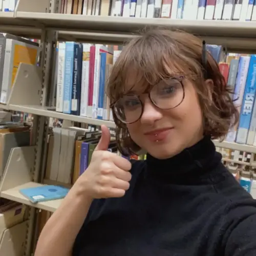 Danita Mapes '23 gives a thumbs up among the shelves in Landman Library