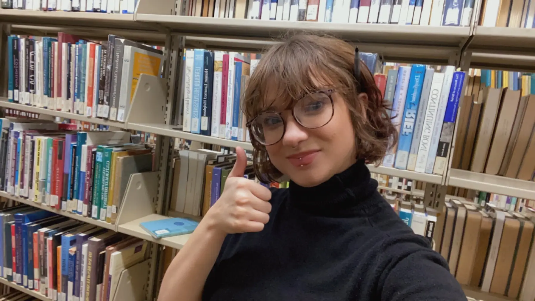 Danita Mapes '23 gives a thumbs up among the shelves in Landman Library