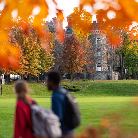 A view on the Grey Towers during the fall season with two students walking by in the frame