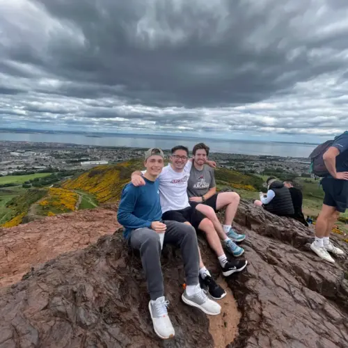 Patrick Ensmenger '23 with two friends seated on a large rock/cliff