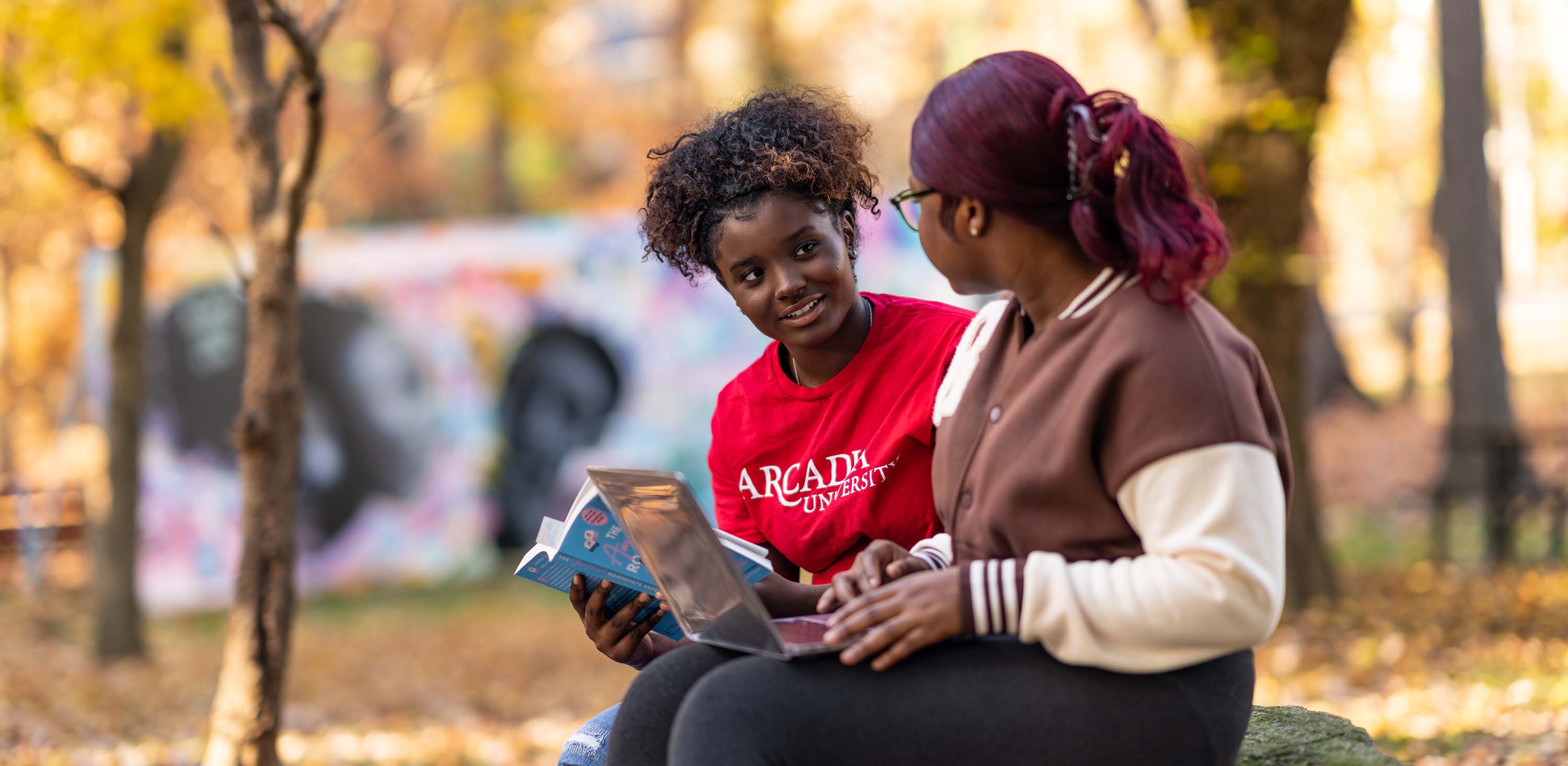 Two students having a conversation outside in the fall season.