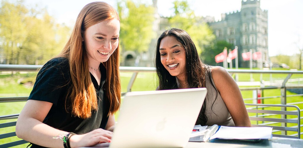 Two students on laptop outside.