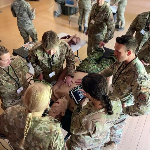 A group of military medics standing over a training dummy to learn medical techniques.