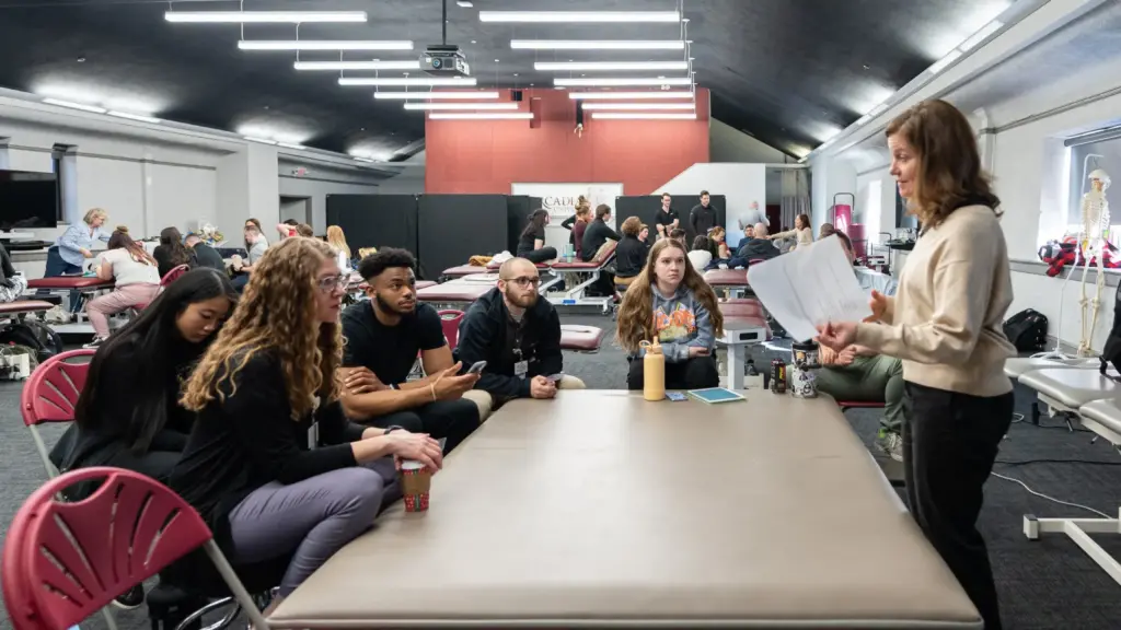 A physical therapy professor instructs students around an exam table