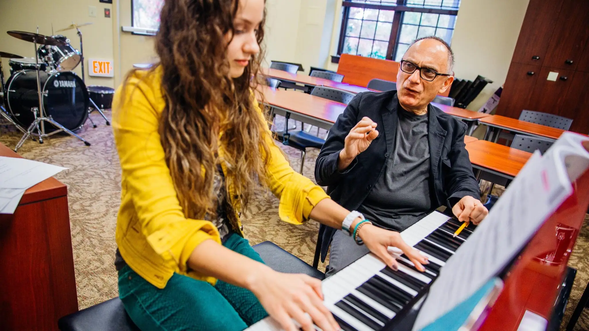 A professor provides instruction to a student playing piano.