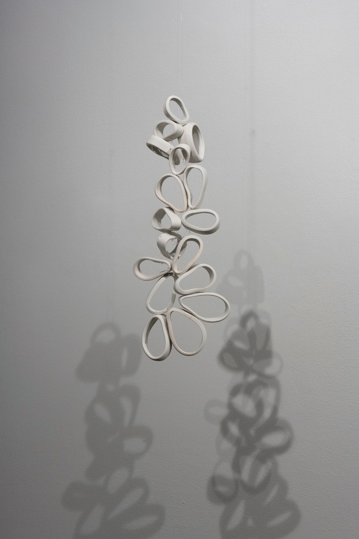 Detail image of a ceramic sculpture made of multiple hollow, oval shaped rings suspended from the ceiling