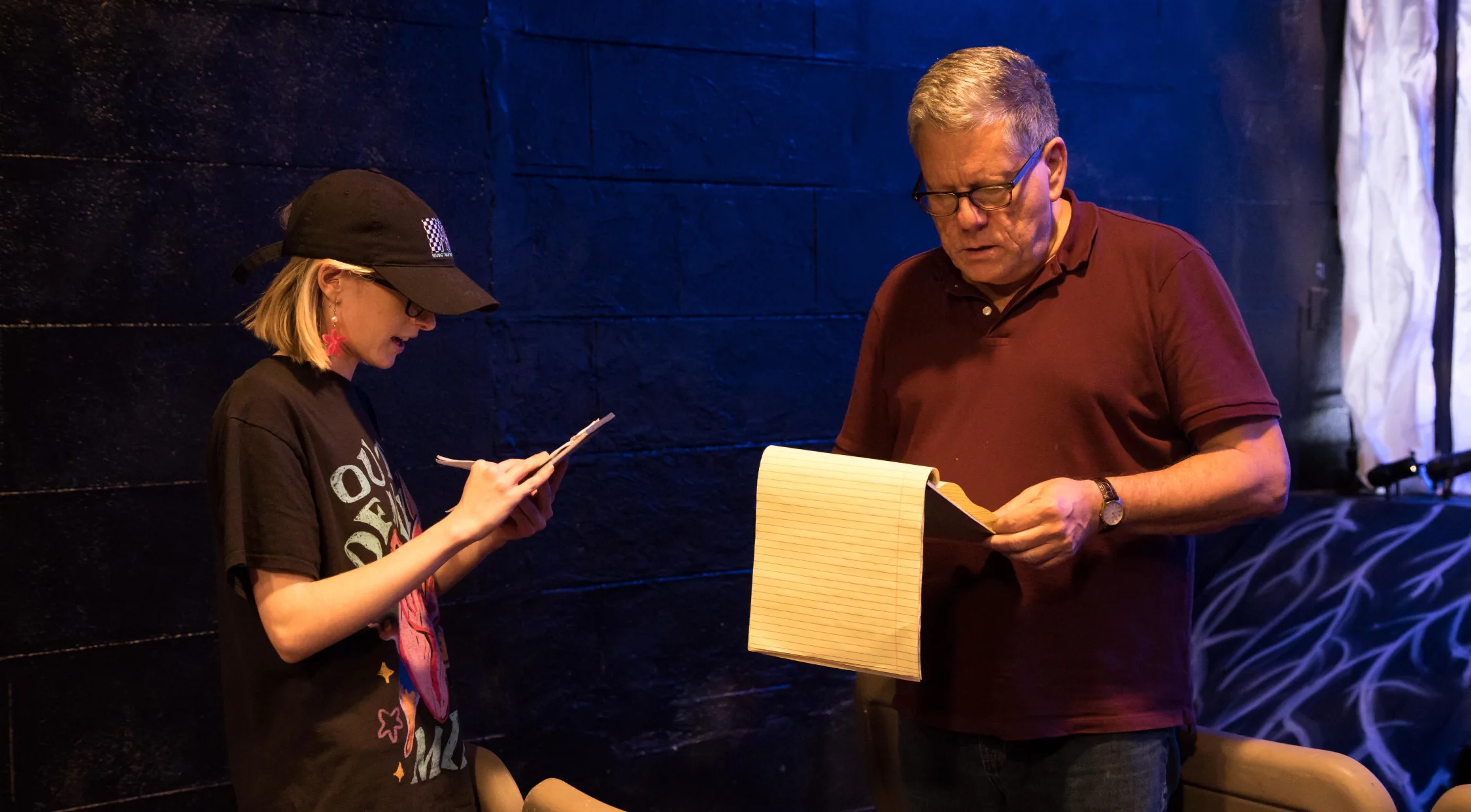 Two people behind stage reading through notes and material.