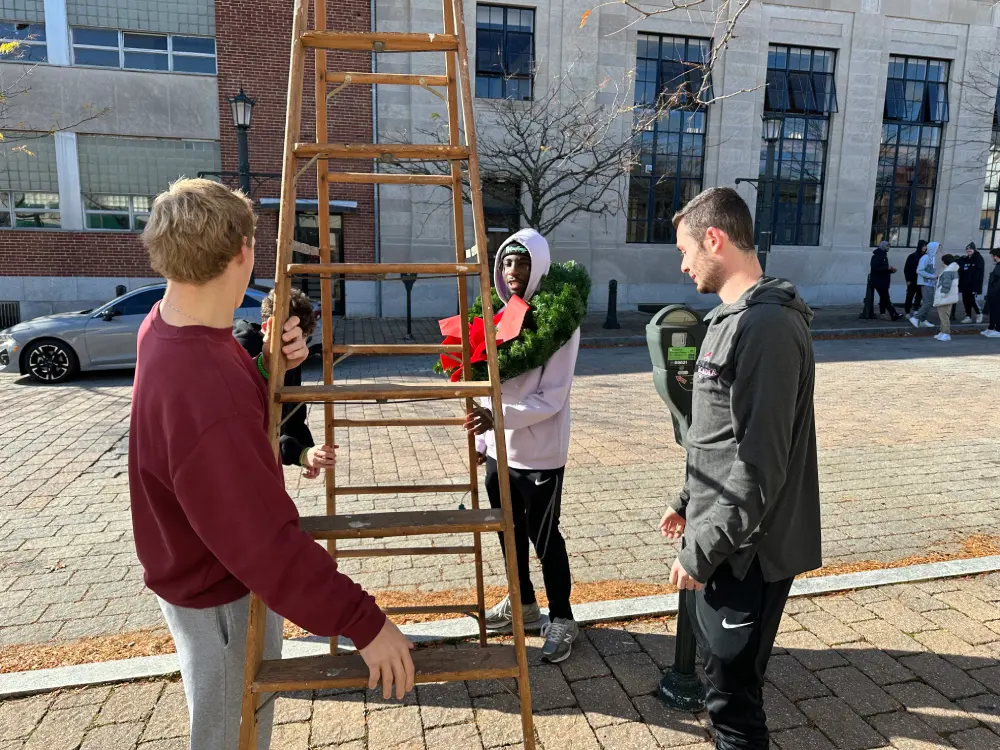 Students setting up a ladder to decorate a lamp post.
