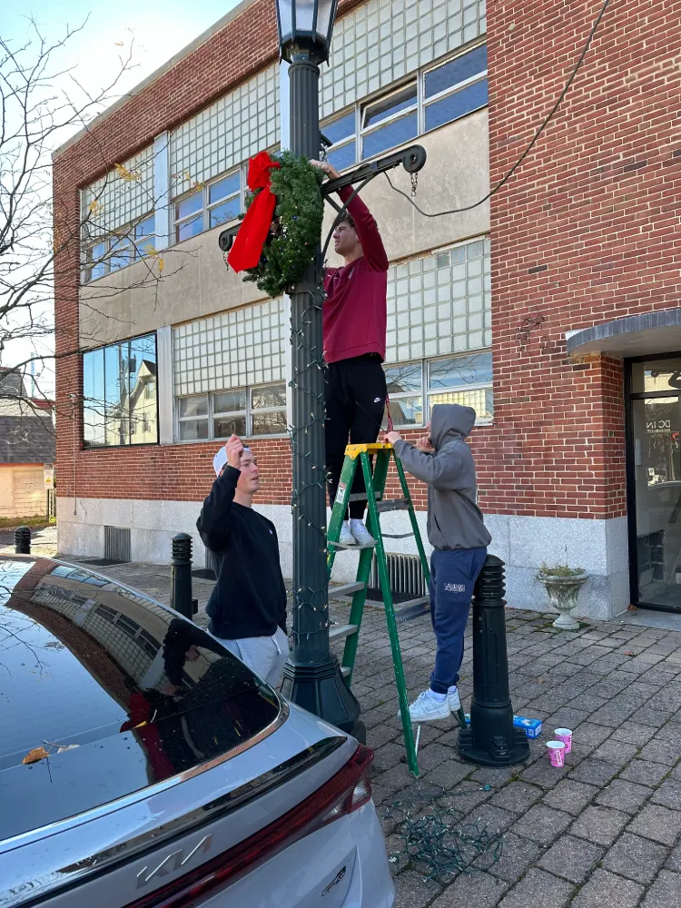 Students hanging a wreath on a lamp post.