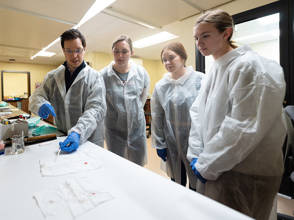 Students watch a forensics professor conduct a lab test.