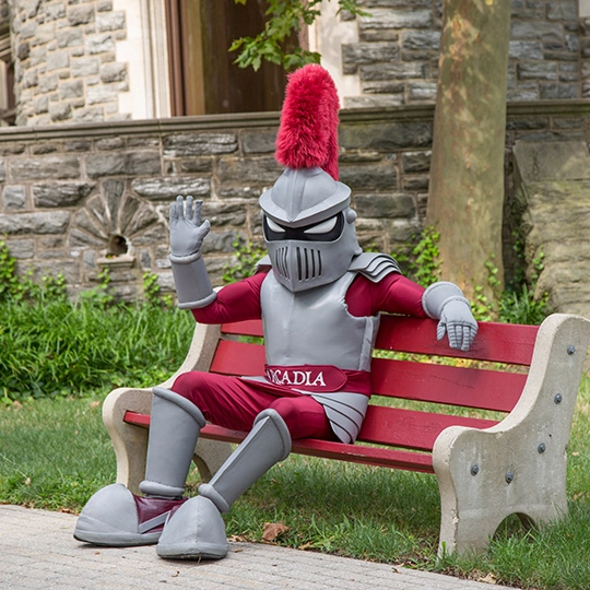 Archie, the mascot sits on a park bench in front of the castle.