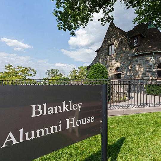 The sign in front of the cobblestone Blankley Alumni House building.