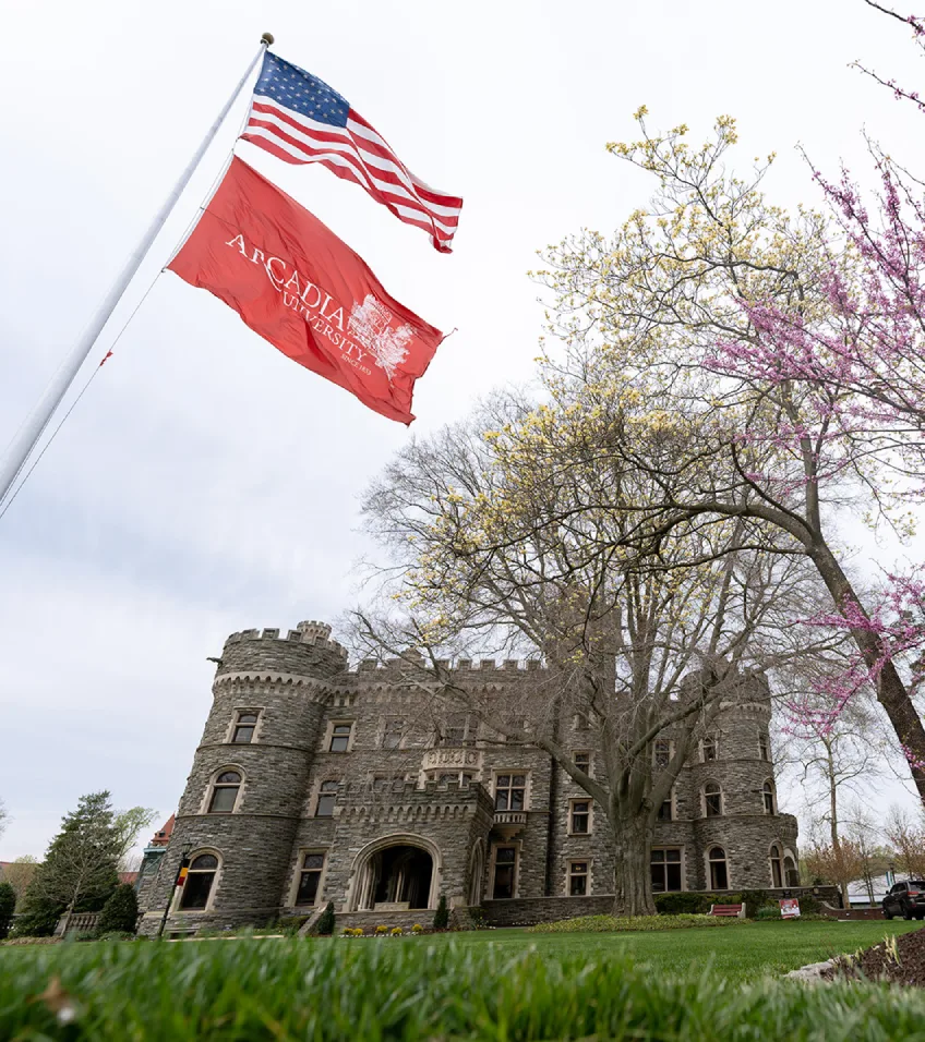 Grey Towwers Castle on a cloudy spring day with a red Arcadia flag and US flag waving.
