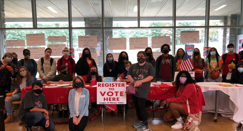 Students crowd over a table of red, white and blue during the 2020 election to encourage voting.