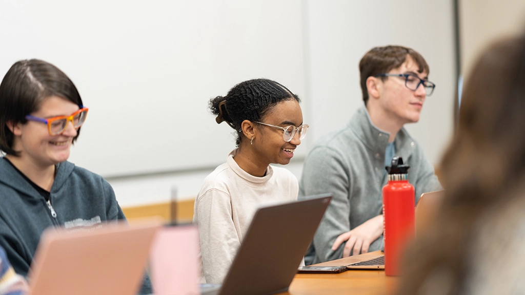 Undergraduate students take notes and smile in a classroom at Arcadia.