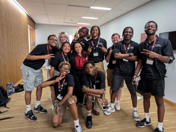 The team from Welcome to Arcadia wearing all-red poses with Archie, Arcadia's mascot.