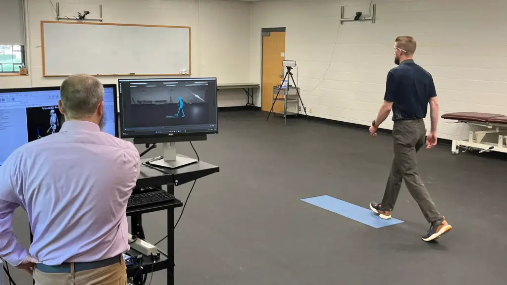 Two men conduct a walking test using computers and cameras in the physical therapy department.