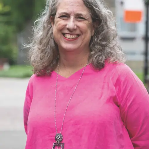 Stacey Downey ’88 stands outside on campus with leafy trees and a flag in the background.