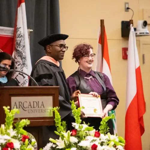 A student holding up their award with faculty member