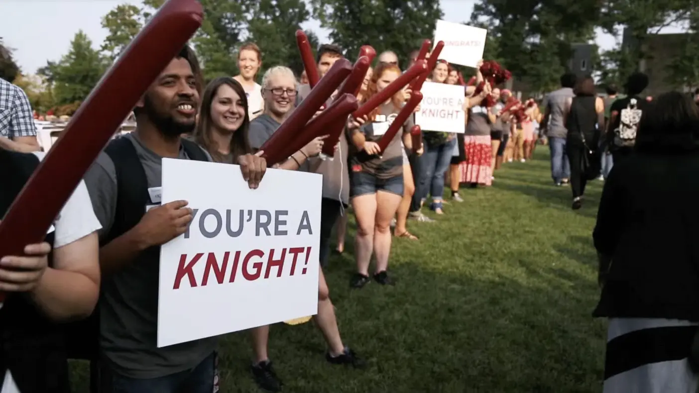 Different people celebrating and holding up a sign saying "You're a Knight!"