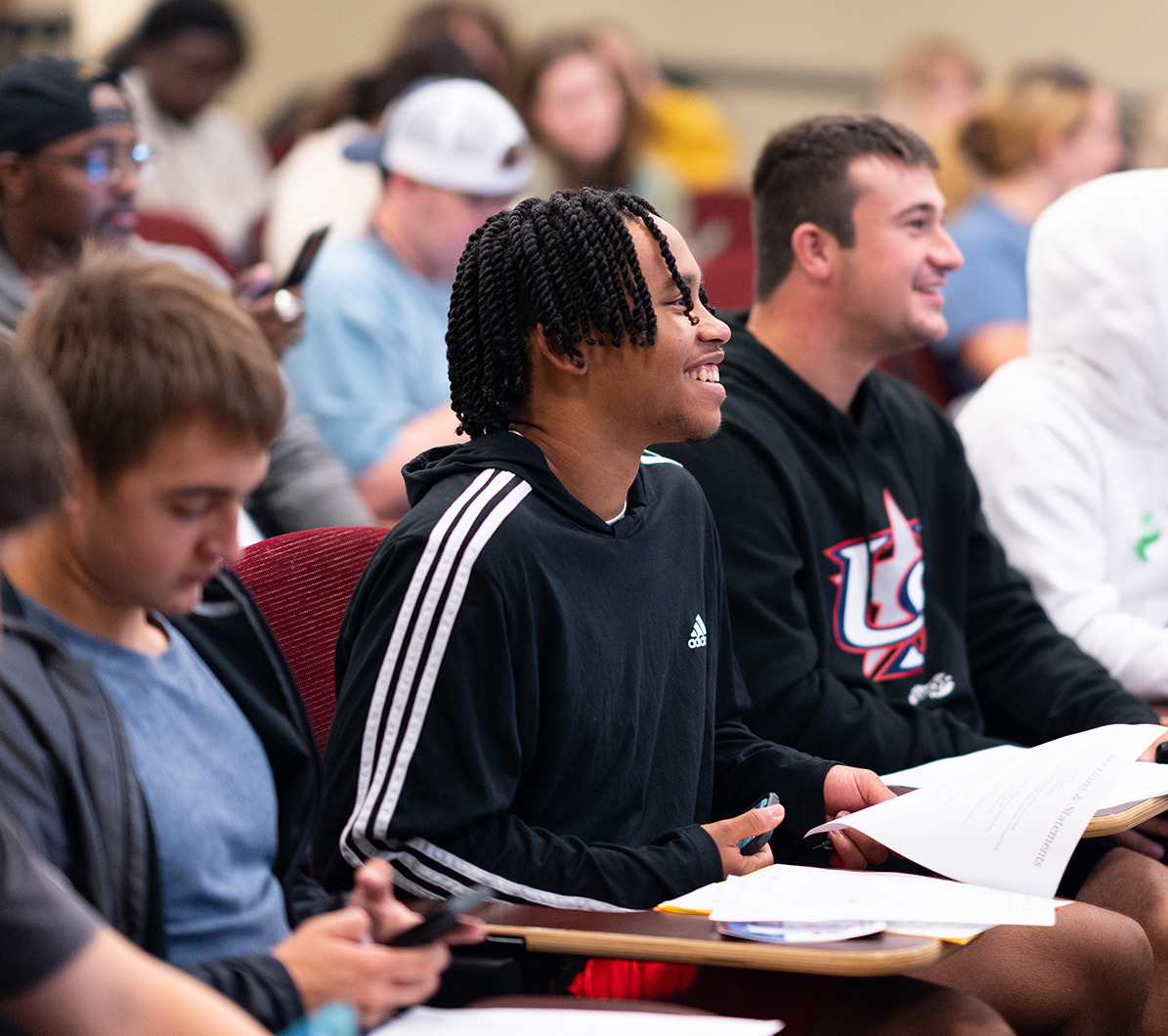 A student smiles as he sits with others in aclassroom.