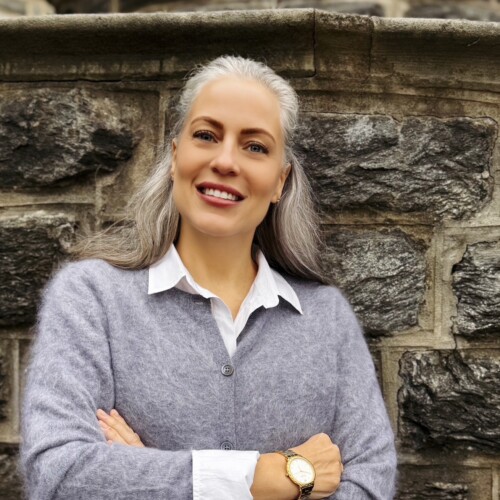 woman with silver and white hair smiling with her arms crossed in front of a stone wall