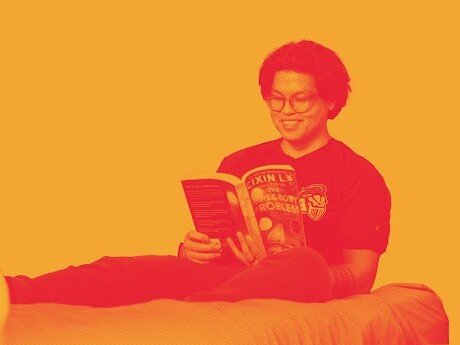 Lee Conlu '25, sitting on a bed reading.