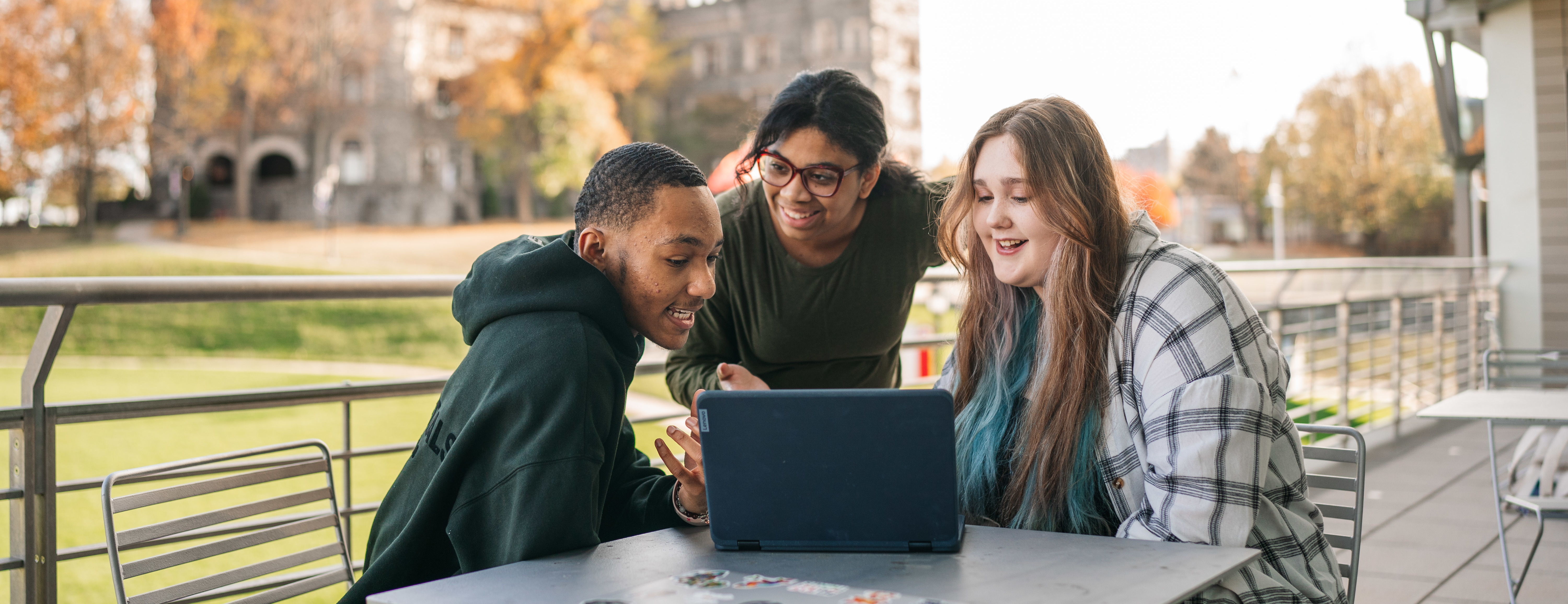 Three Arcadia students looking at a computer on the upstairs patio of The Chat on campus.