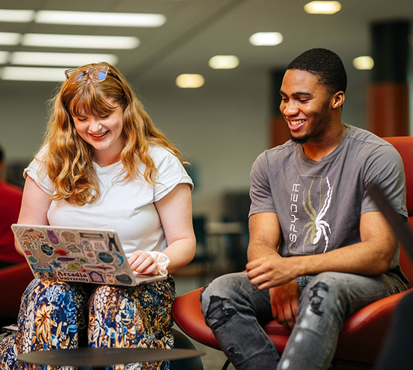 Two undergraduate students smile as they work toegether on a laptopcomputer.