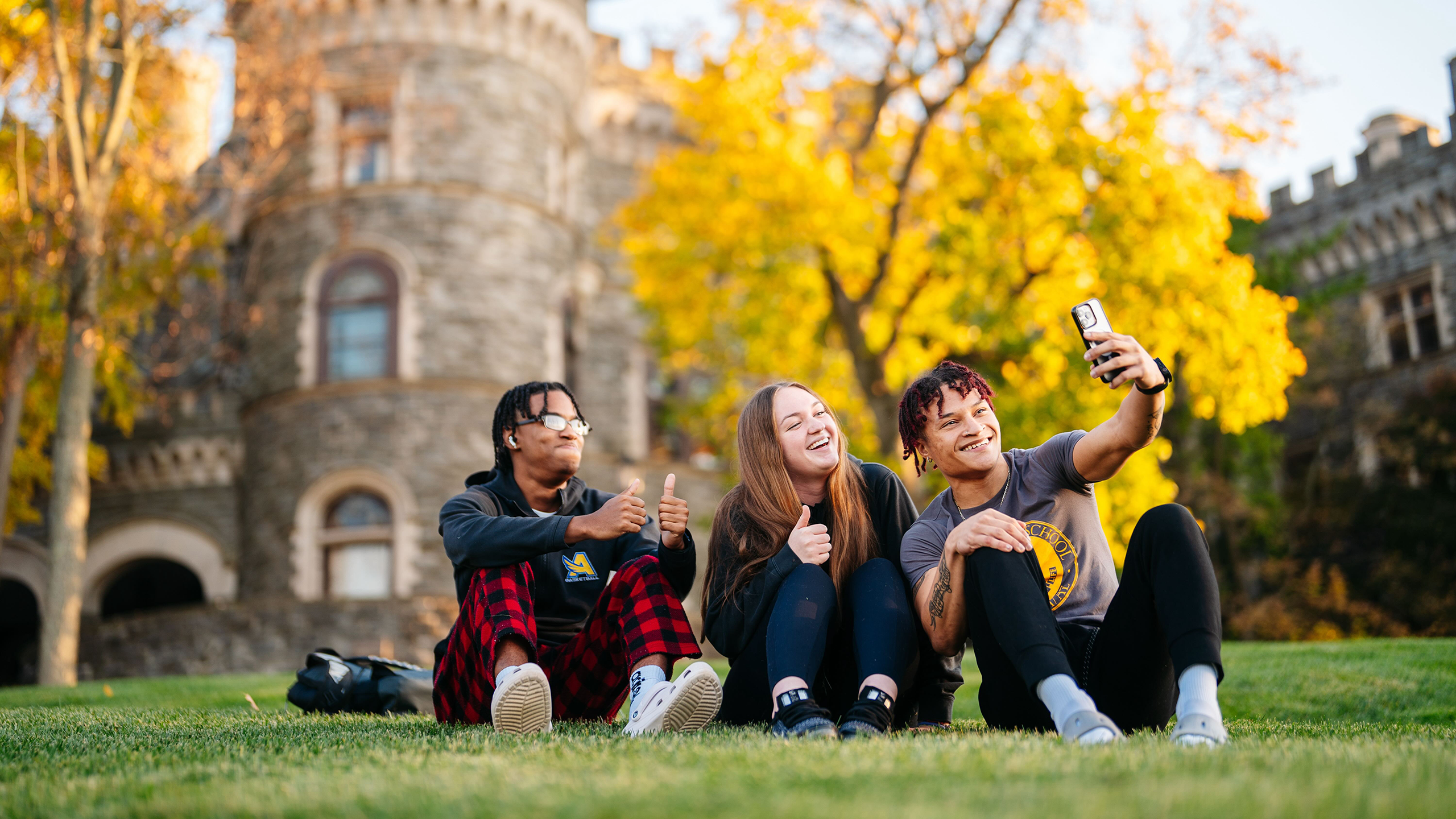 On a bright fall day full of color, three undergraduate students take a selfie in front of Grey's Castle.