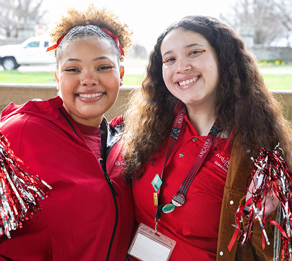 With a splash of sun in the background, two students smile as they wear Arcadia red.