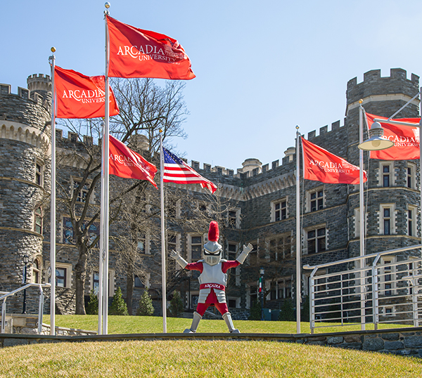 Archie stands proudly waving his arms with the castle and flying flags in the background.