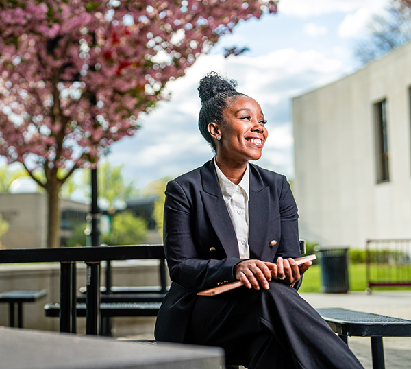A graduate student sits on a picnic table bench and holds a computer.