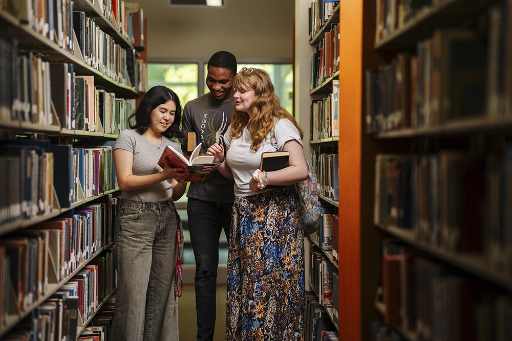 Three students look at a book in the library.