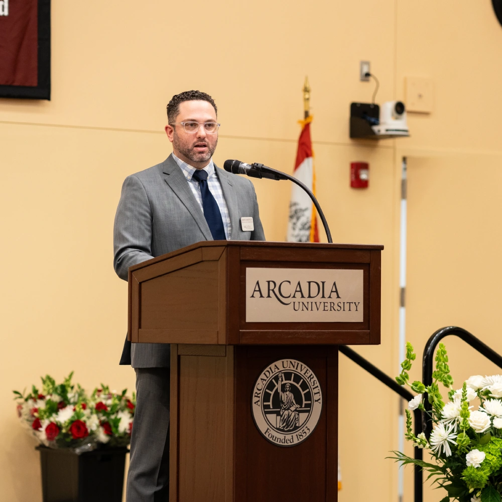 Adam Planamento '12 speaking at a podium.
