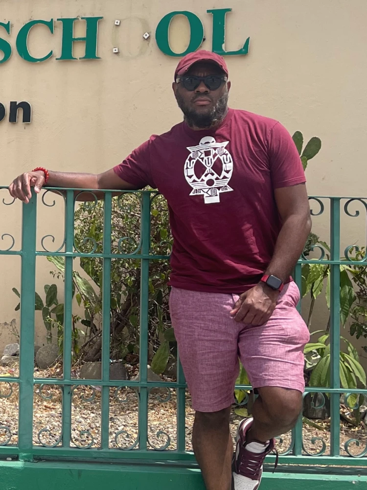Gene Bazemore '00 leaning against a green fence.
