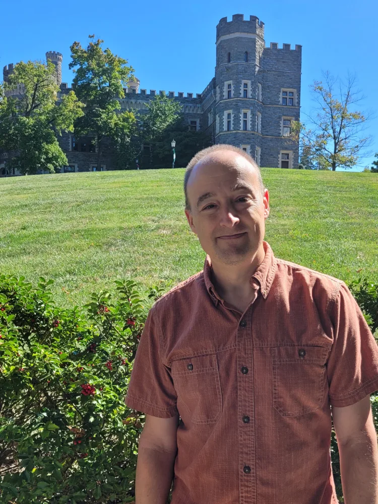 Ken Samen '92 stands on campus with Grey Towers Castle in the background.