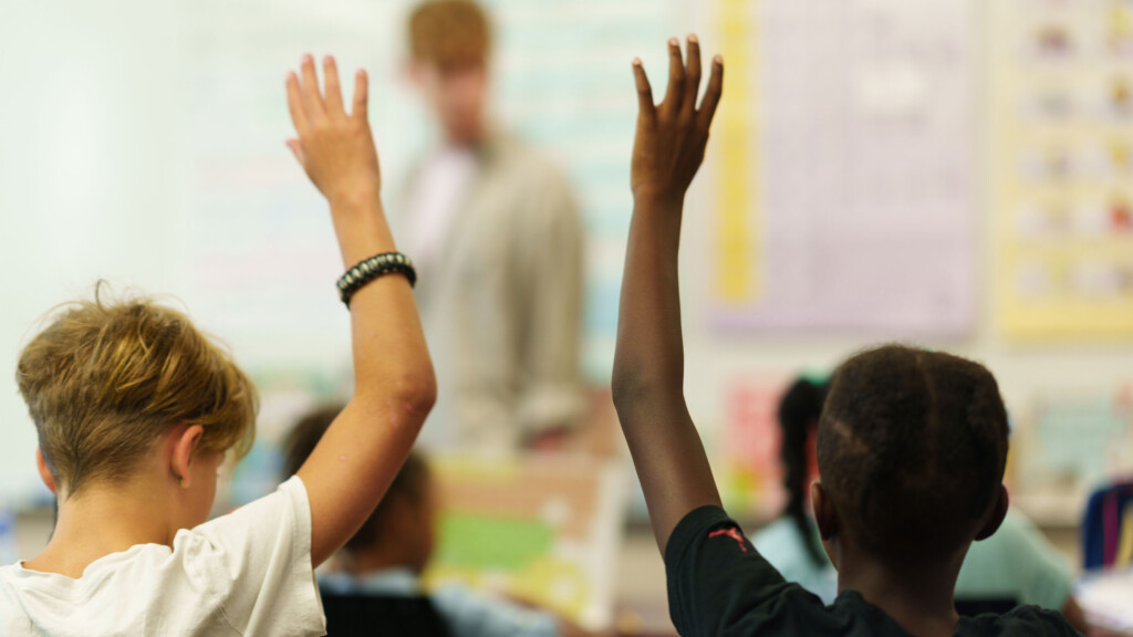 Two students with their hands raised in the classroom