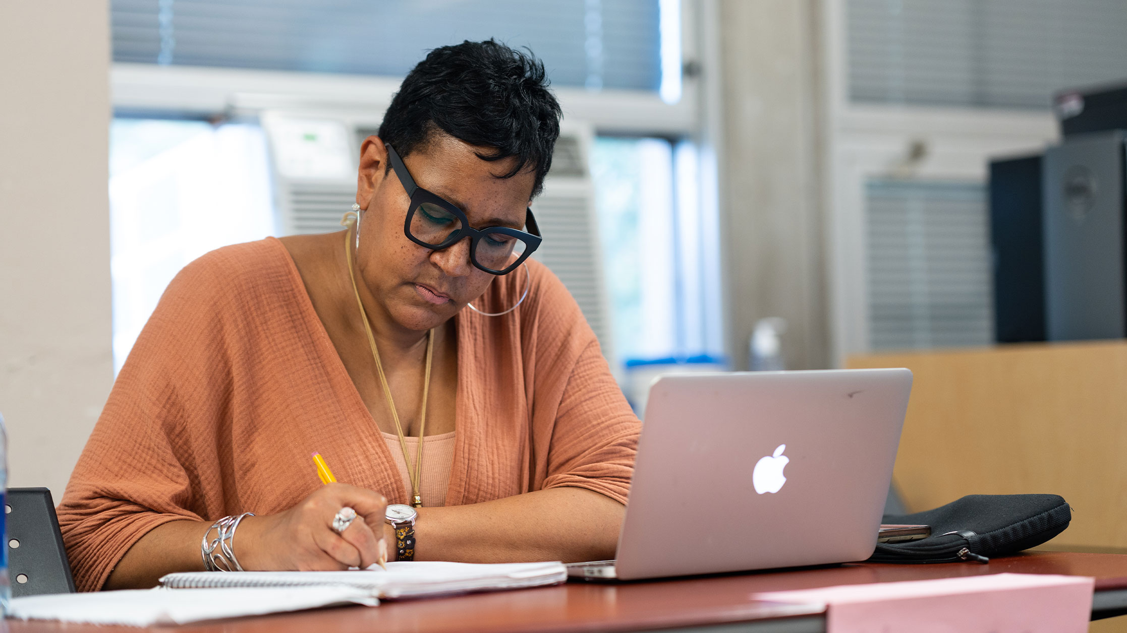 Teacher at desk grading papers in front of Apple laptop